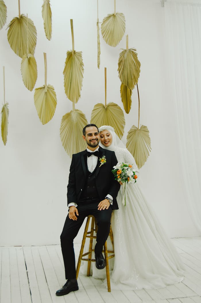 A bride in a white dress and groom in a tuxedo posing against artistic decor.